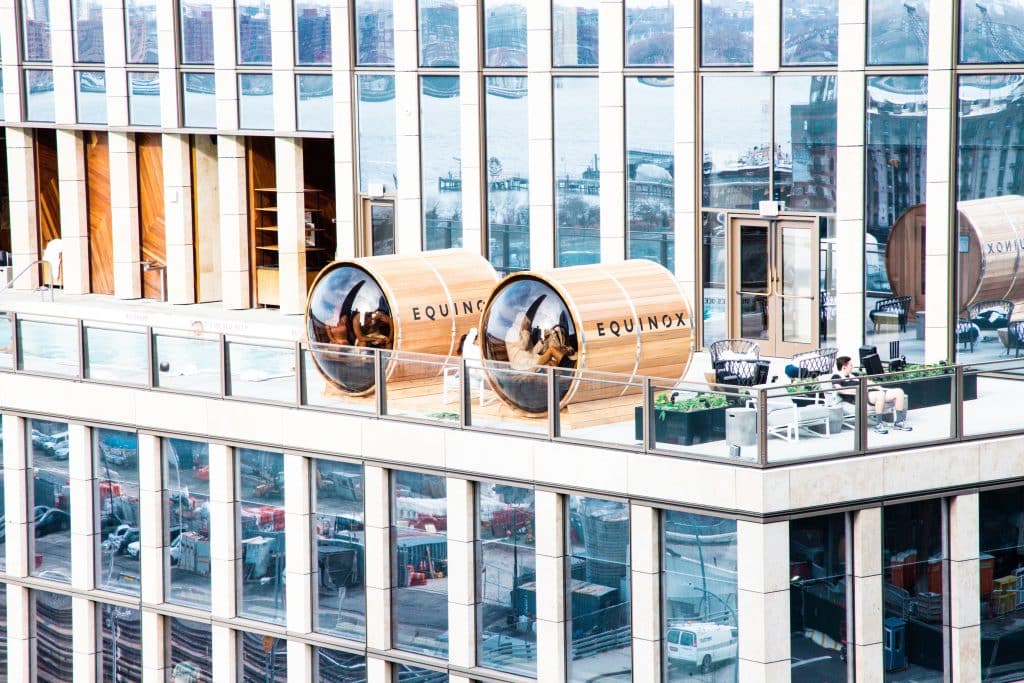 Luxuriöse Rooftop-Terrasse mit EQUINOX-Saunen, moderner Glasarchitektur, stilvollen Outdoor-Möbeln und Panoramablick über die Stadt – Wellness und Entspannung über den Dächern.
