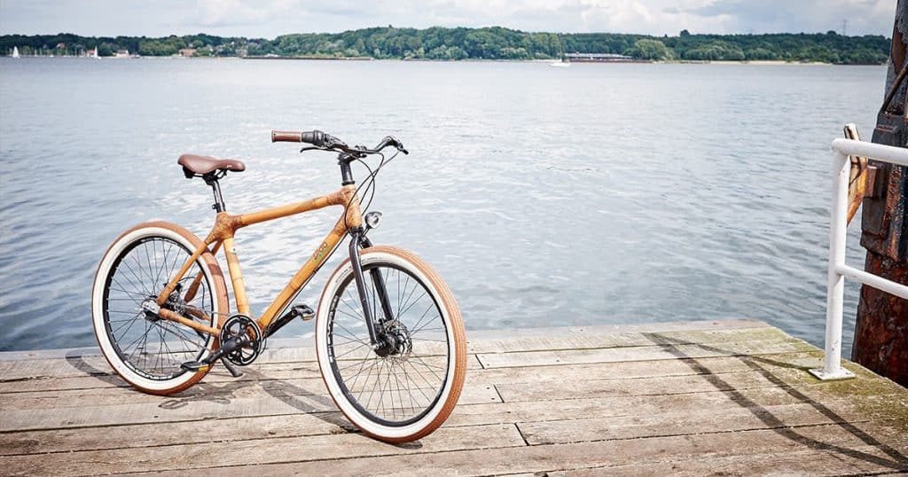 Holzfahrrad mit weißen Reifen auf einem Steg am See – Symbol für nachhaltige Mobilität und umweltbewusste Hotellerie.