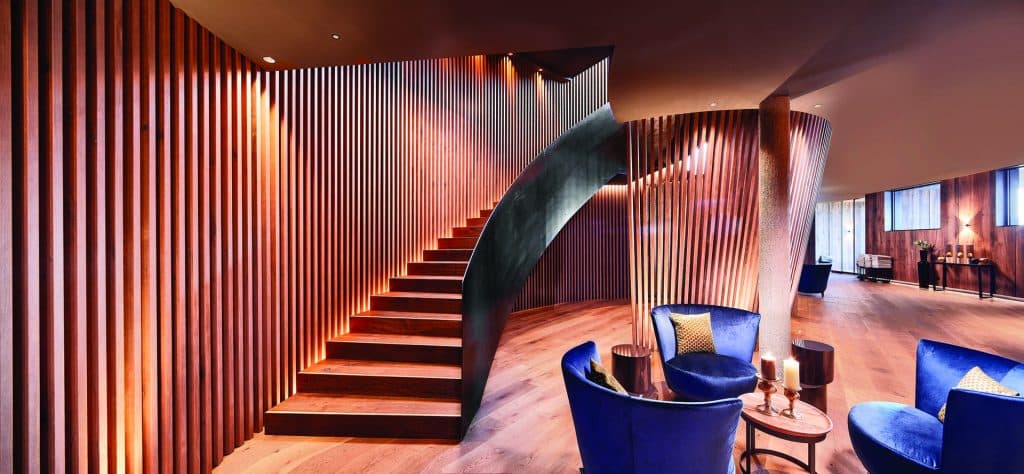 Elegante Hotellobby mit geschwungener Holztreppe, blauen Samtsesseln und stilvoller Einrichtung – modernes Interior-Design in der Hotellerie.